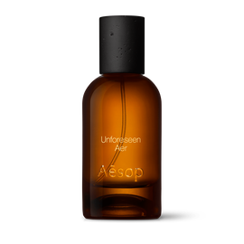 Bernsteinfarbene Flasche des Aesop Unforeseen Aer Eau de Parfum aus Glas mit schwarzem Verschluss vor weißem Hintergrund.
