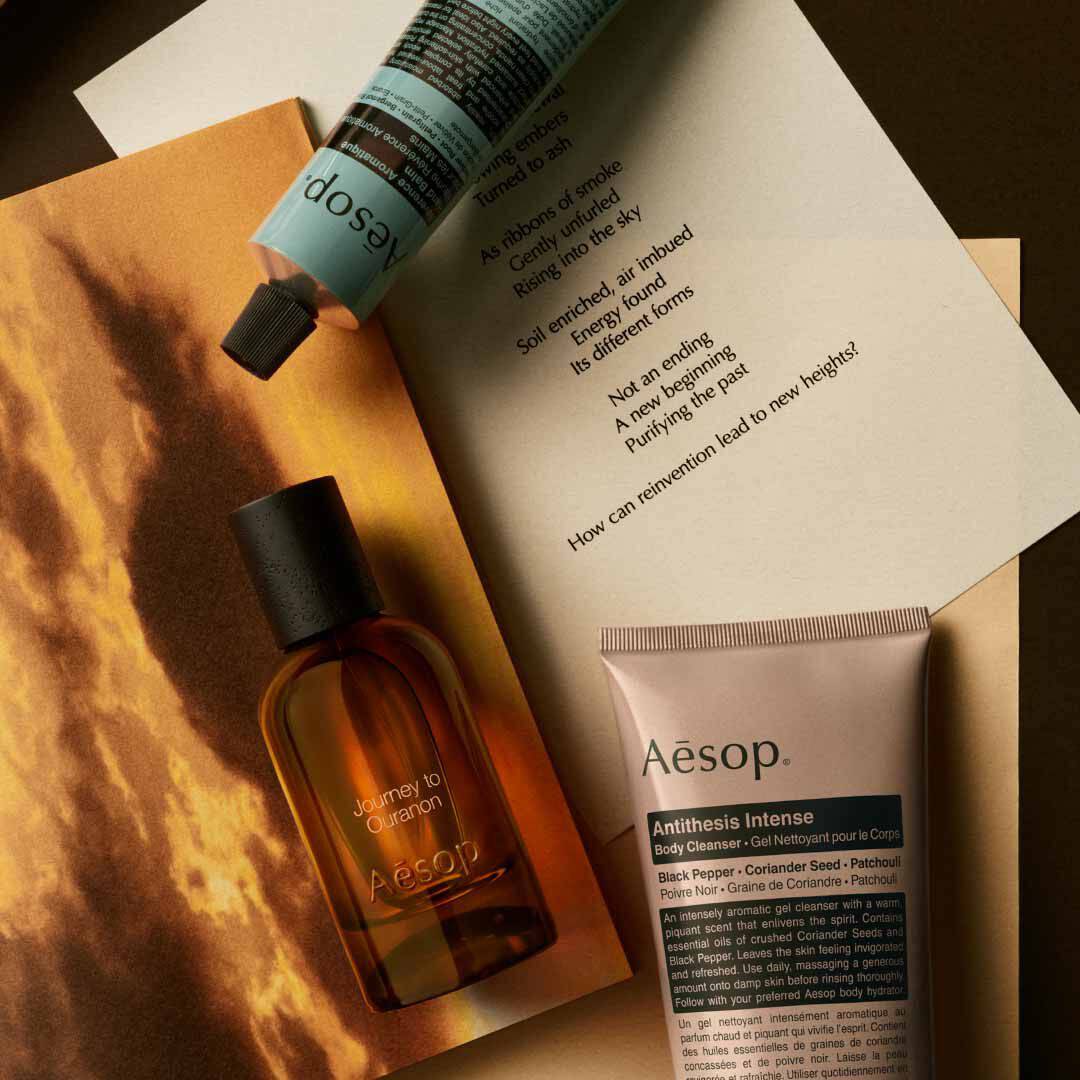 Aesop Journey to Ouranon Flakon mit Pumpspender und Schlauch, arrangiert auf Papieren mit einem leuchtenden Landschaftsbild.
