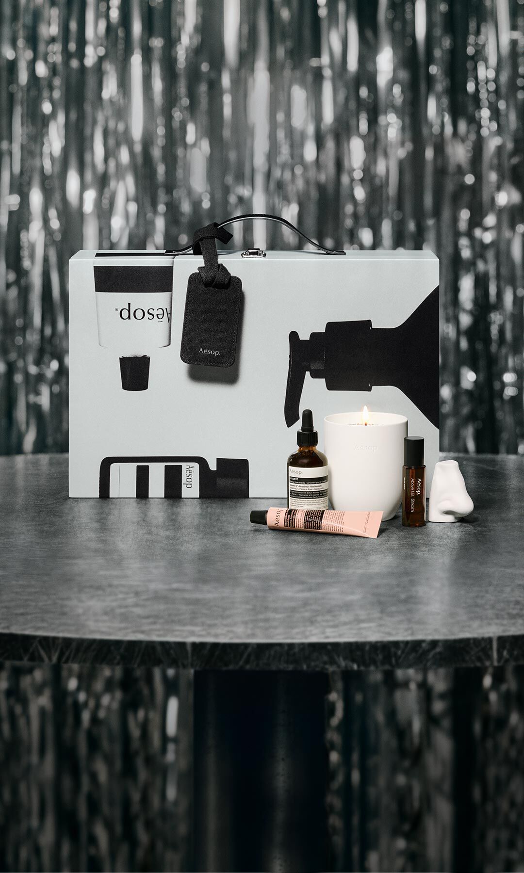 Aesop-Geschenkset und Hautpflegeprodukte auf einem Tisch vor festlich beleuchtetem Hintergrund.