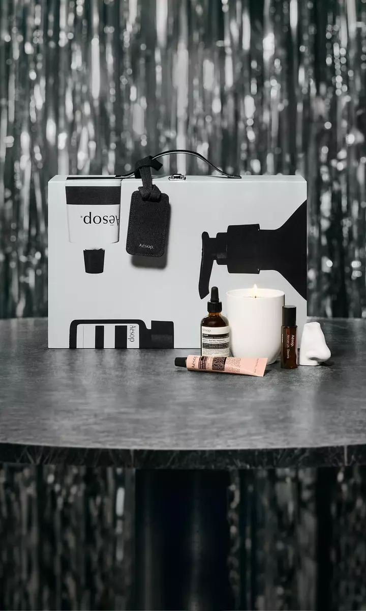 Aesop-Geschenkset und Hautpflegeprodukte auf einem Tisch vor festlich beleuchtetem Hintergrund.