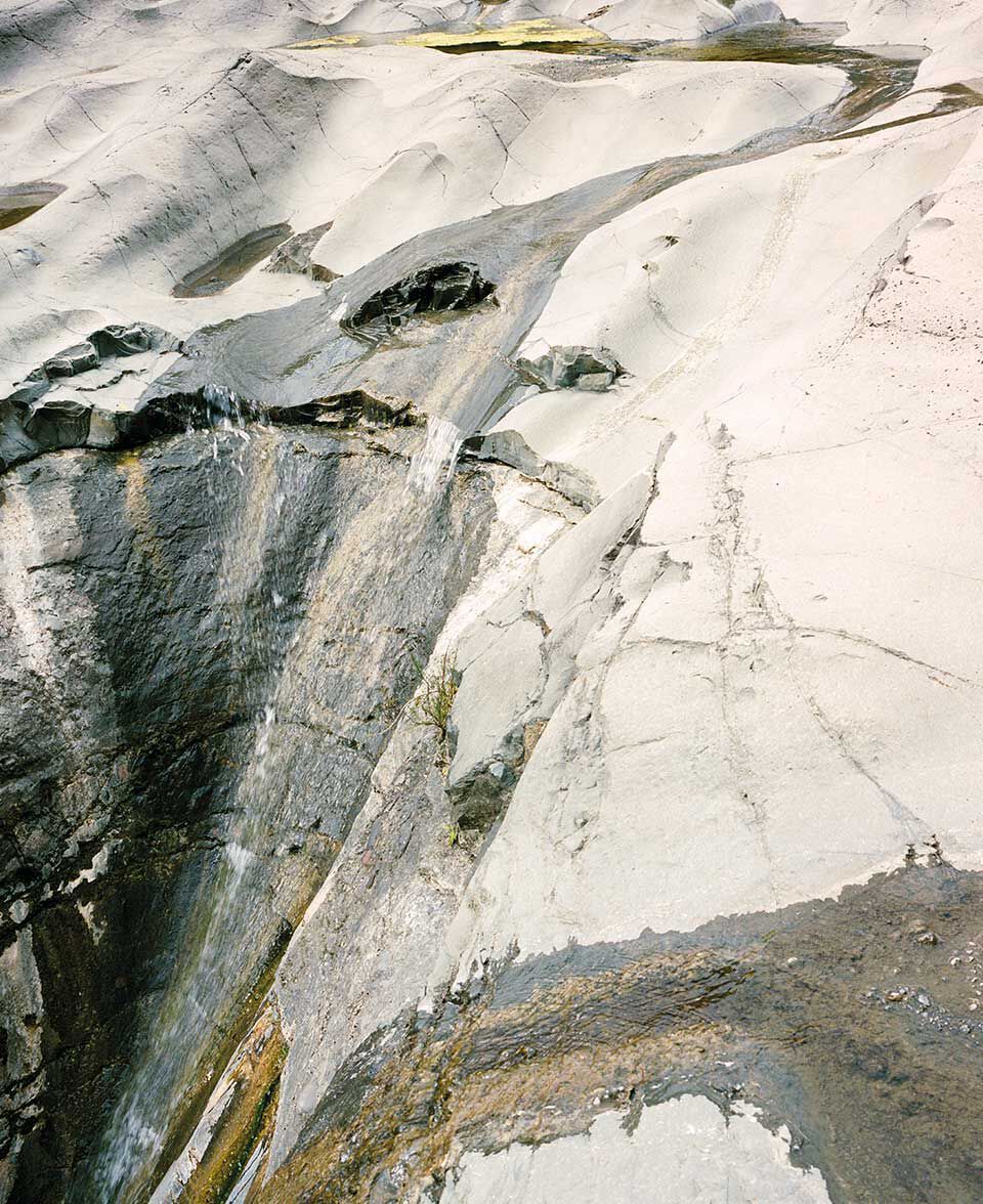 Blasse, verwitterte Felswand mit fliessenden Mineralmustern und Streifen.