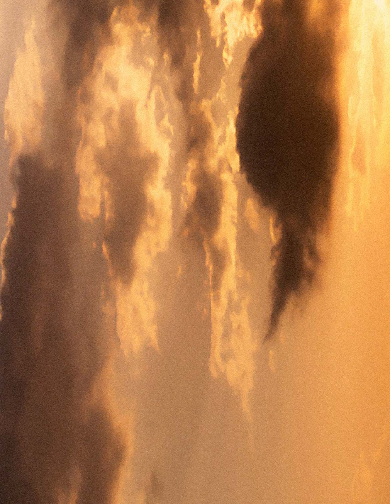 Goldener Sonnenuntergangshimmel mit geschichteten Wolken in warmen Bernsteintonen, sanft gestreutem Licht und dunkleren Wolkenformationen, die die Szenerie durchziehen.