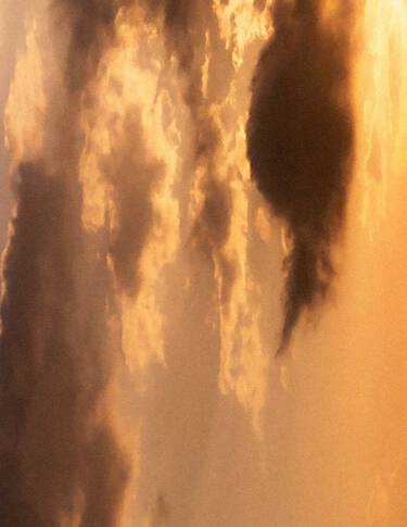 Goldener Sonnenuntergangshimmel mit geschichteten Wolken in warmen Bernsteintonen, sanft gestreutem Licht und dunkleren Wolkenformationen, die die Szenerie durchziehen.