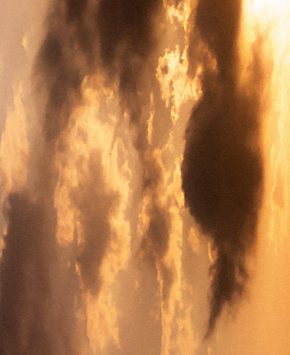 Leuchtende Wolkenformationen in warmem orangefarbenem Licht, die an Rauch und einen vom Feuerschein erhellten Himmel erinnern.