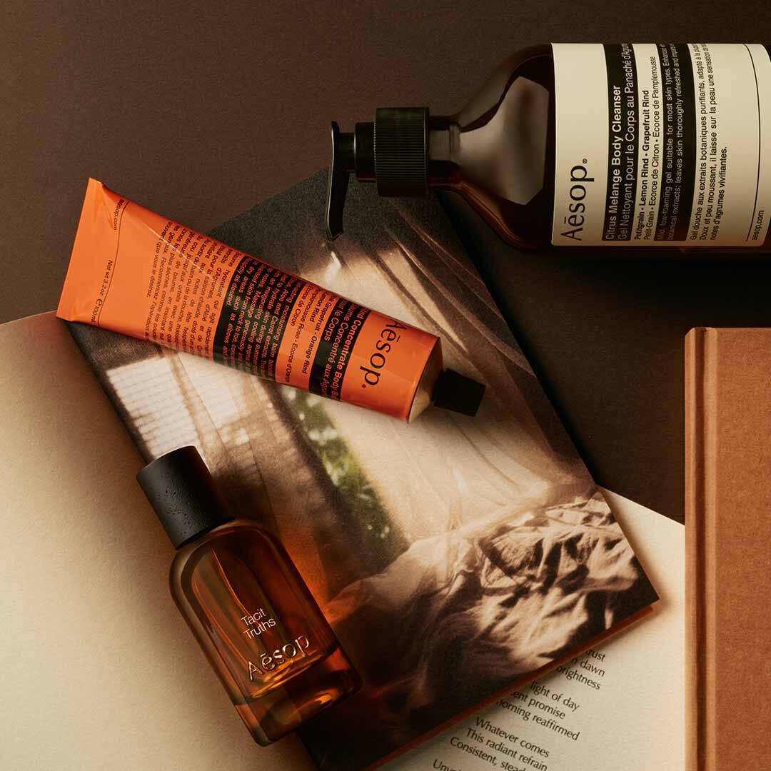 Aesop Tacit Truths Flakon mit Pumpspender und orangefarbenem Schlauch, arrangiert auf Papieren mit einem monochromen Bild.