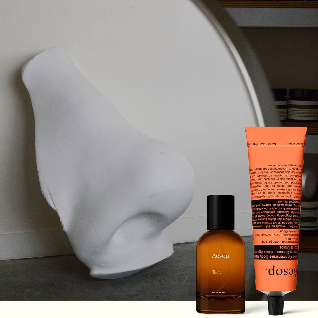 Bernsteinfarbene Parfumflasche und korallenfarbene Handcreme neben einer weißen Skulptur
