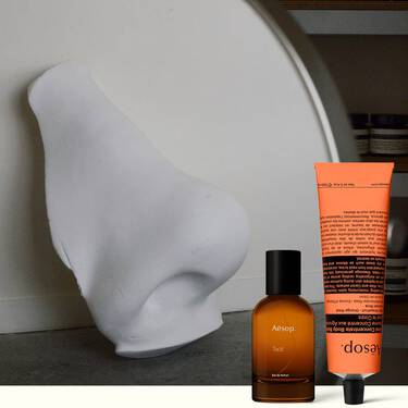 Bernsteinfarbene Parfumflasche und korallenfarbene Handcreme neben einer weißen Skulptur