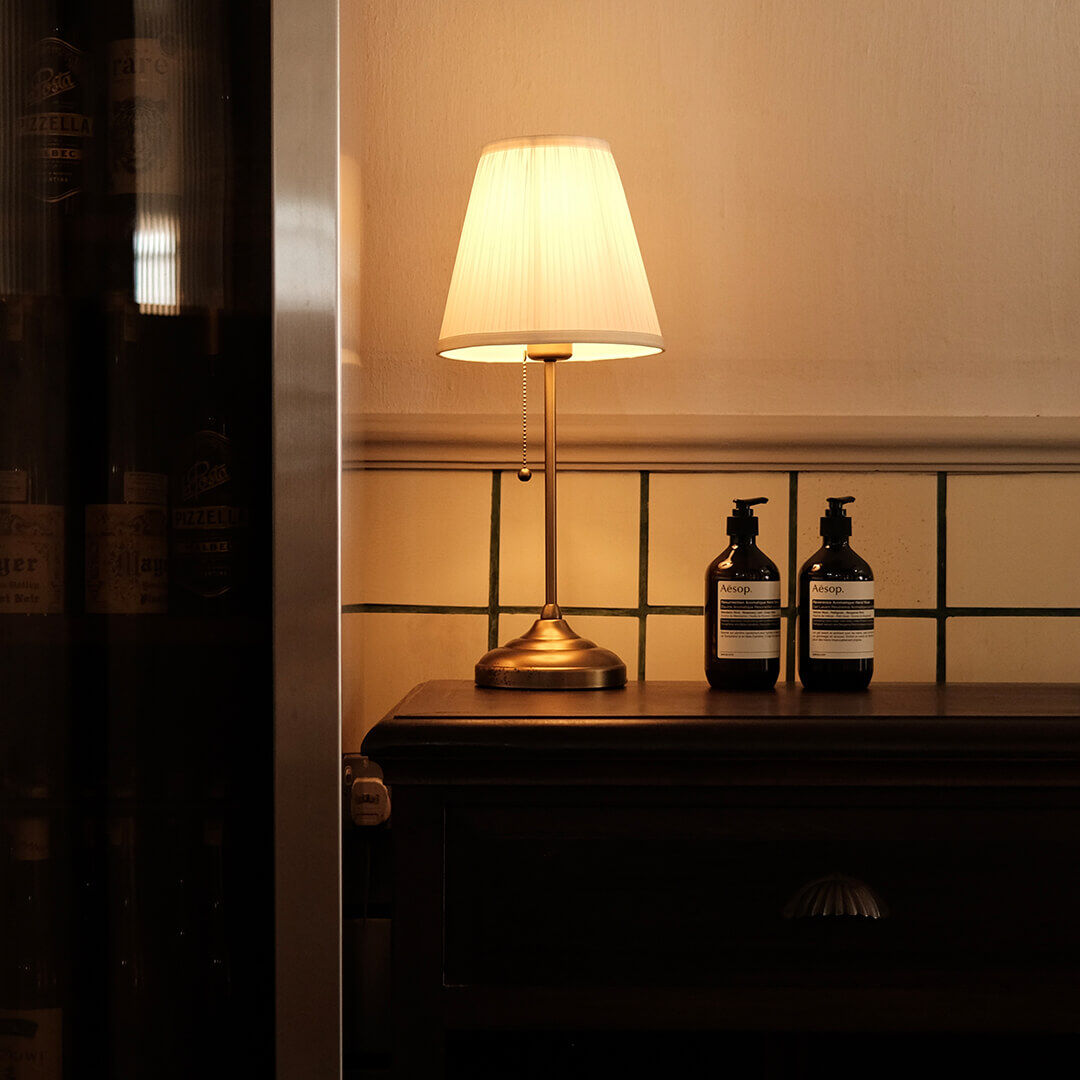 Zwei Aesop-Flaschen auf einem Konsolentisch neben einer antiken Lampe.