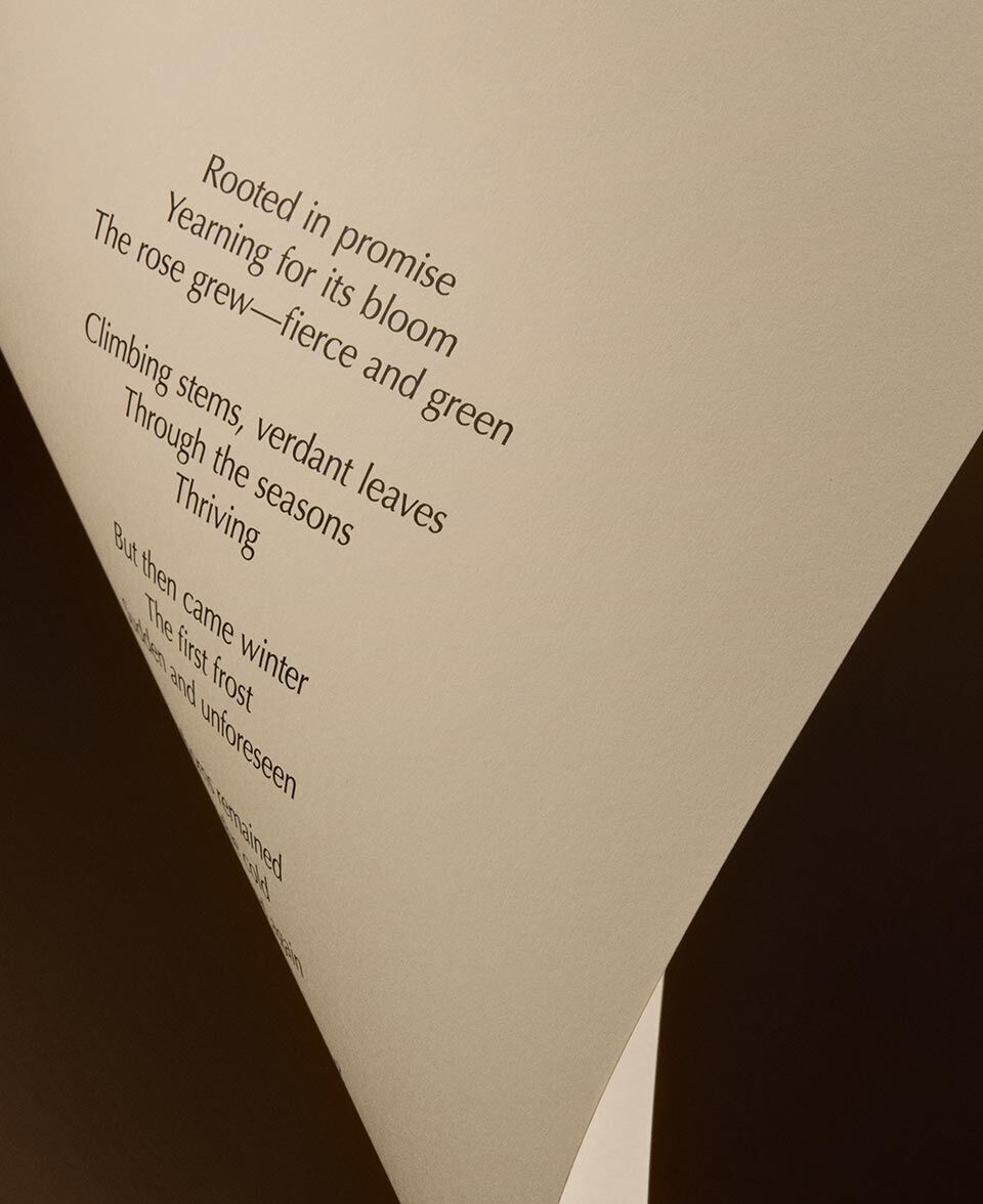 Dreieckige Faltung aus cremefarbenem Papier, die vor dunklem Hintergrund einen Gedichttext zeigt.