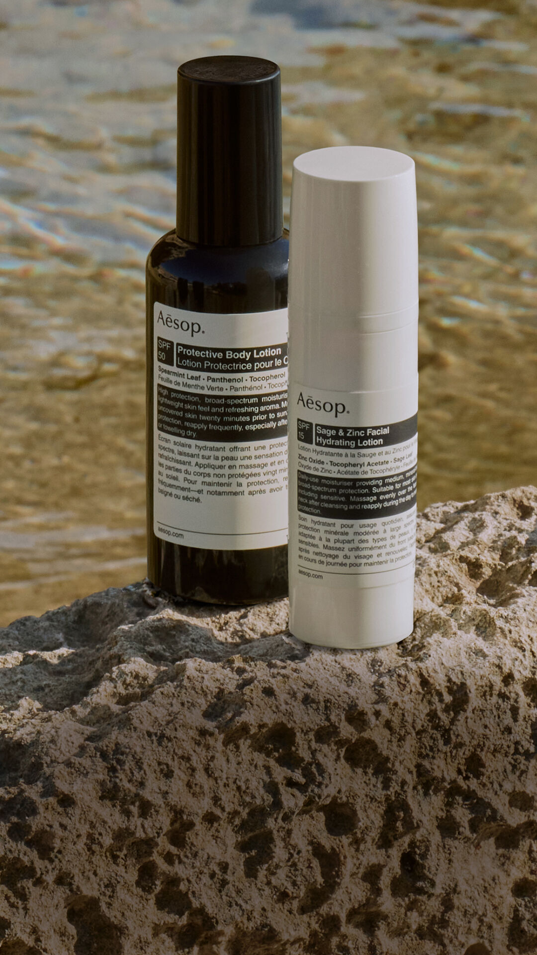 Eine sorgfaltige Auswahl an Aesop Sonnenschutz-Formulierungen, die auf einem Felsen am Meer ruhen.
