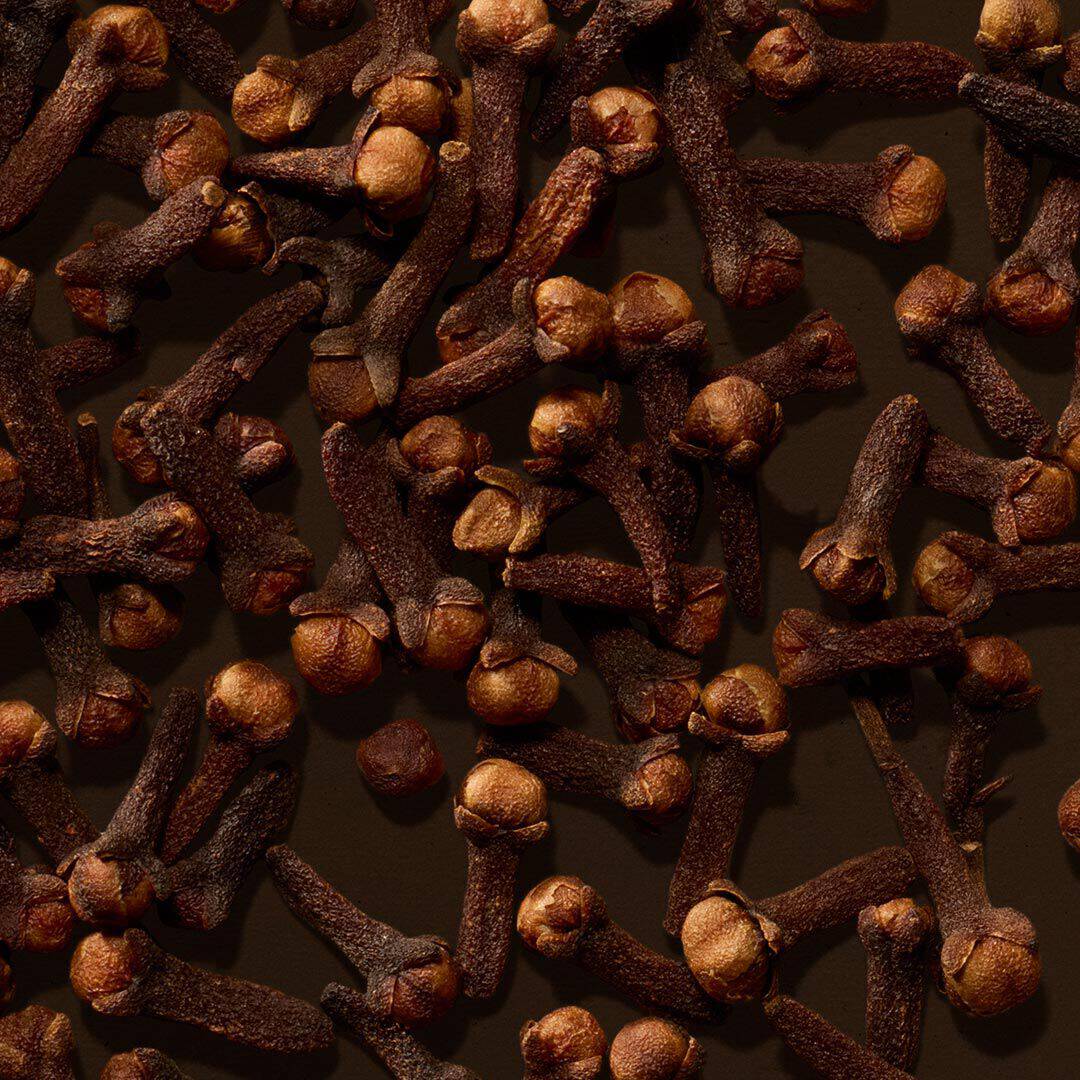 Close-up of cloves scattered across a dark brown surface.